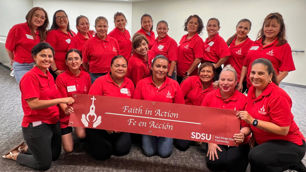 19 Latinas with matching red polo shirts pose with a Faith in Action / Fe en Accíón banner.